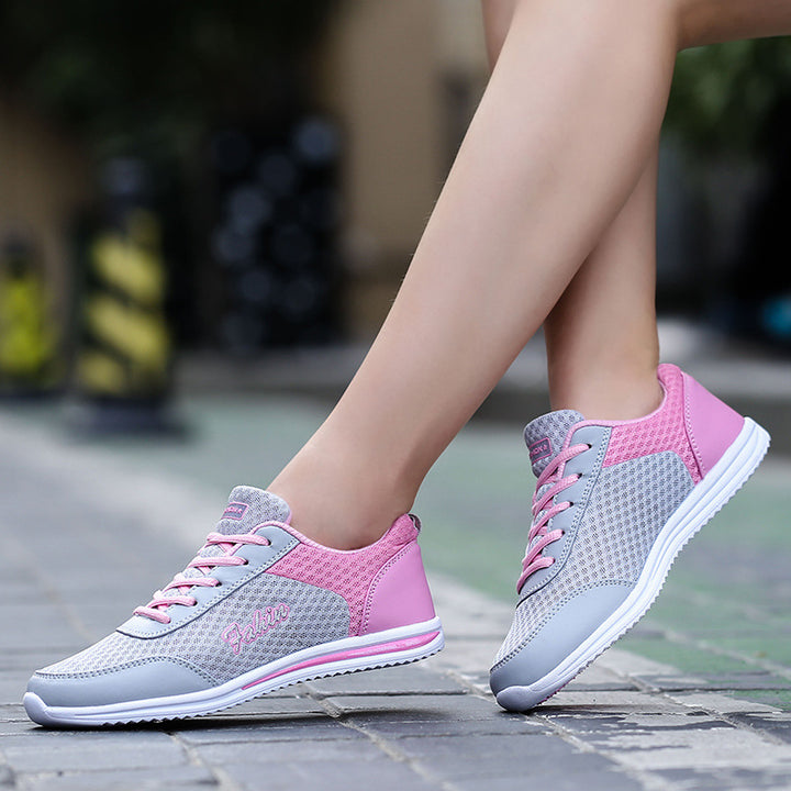 Gray and pink lace-up shoes worn outdoors, showing pink heel panels, gray mesh uppers and white soles beside a stone pavement