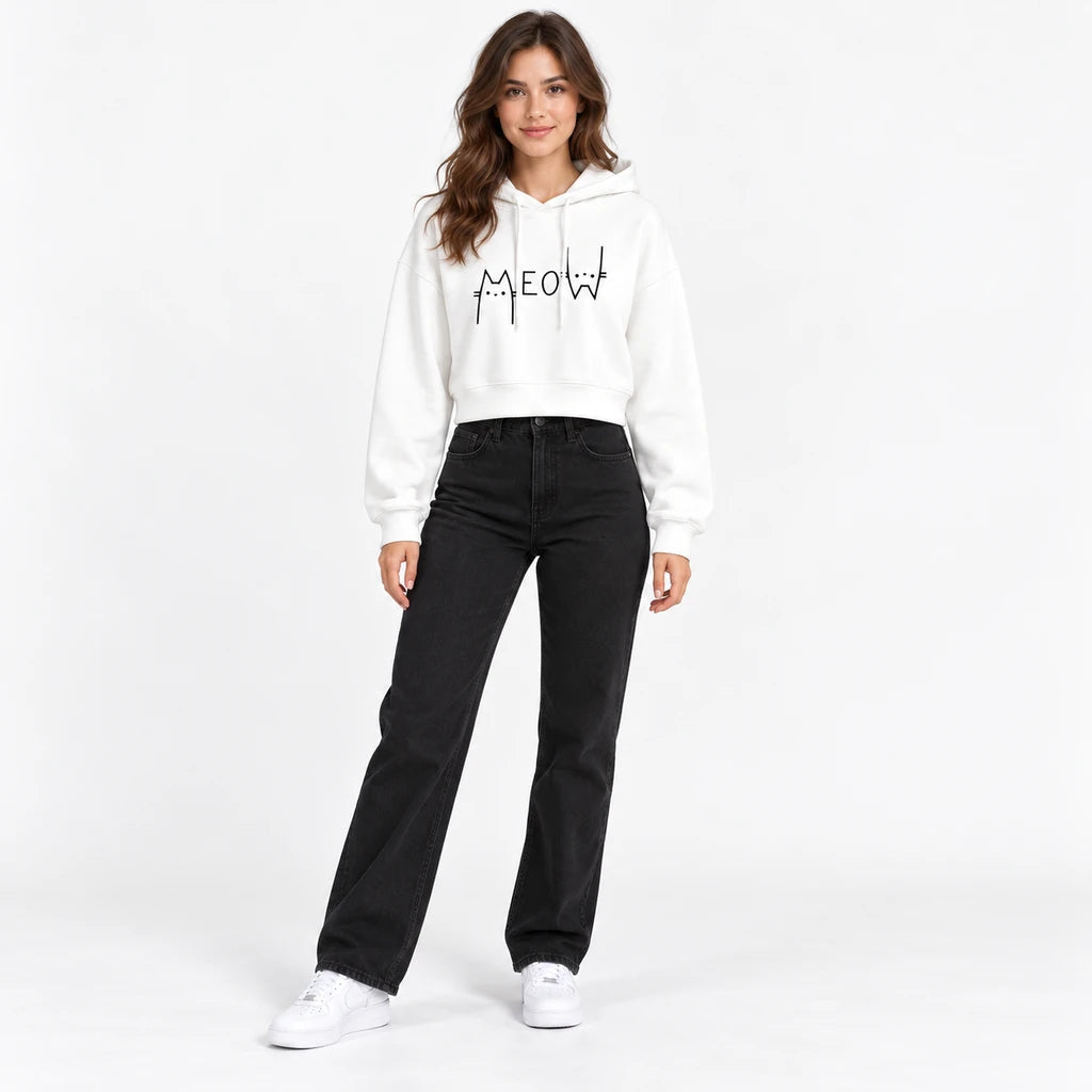 White Meow graphic cropped hoodie on a full-body model with long sleeves and a drawstring hood with black jeans and sneakers.