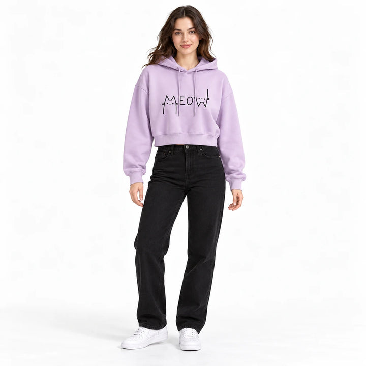 Lilac Meow cropped hoodie on a full-body model with black denim, showing the black cat graphic, long sleeves, and ribbed hem.