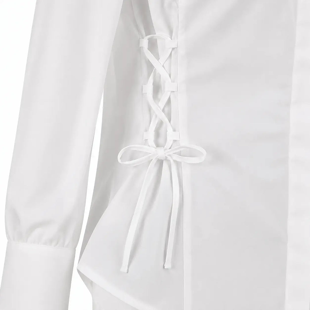 Detail of the white blouse side lacing, showing fabric loops, crossed cord tied bow, waist seam, and curved lower hem detail.