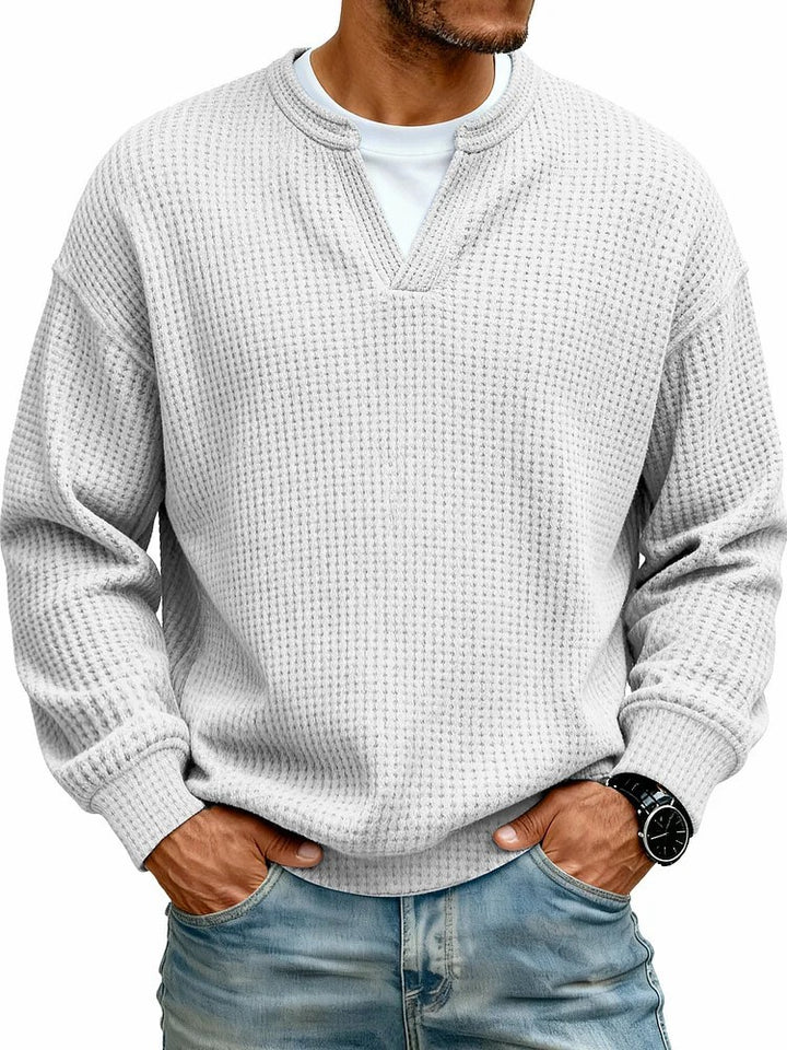 Man wearing a textured light gray sweater and jeans on a white background