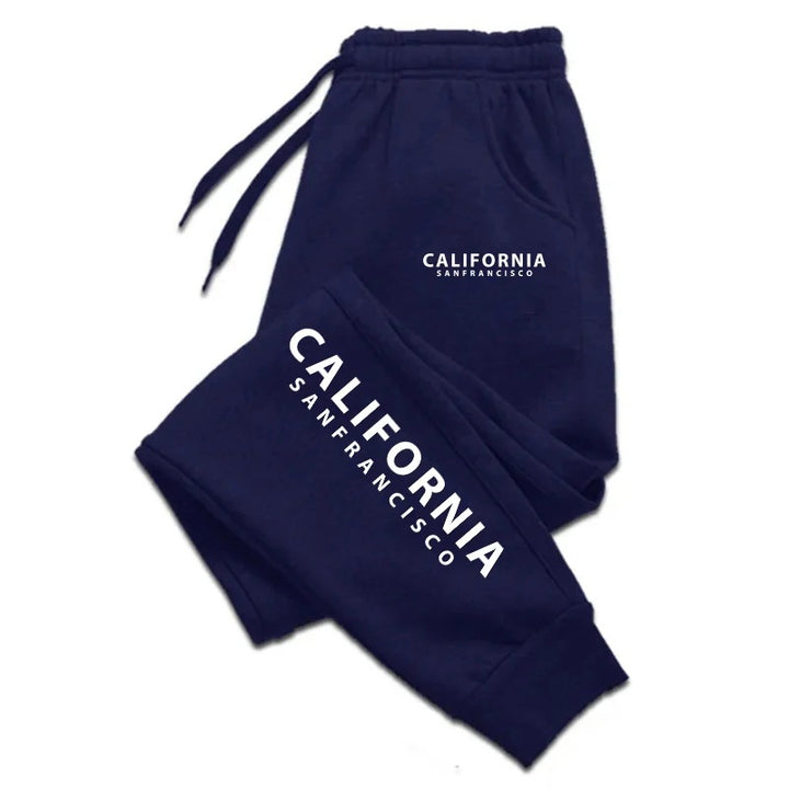 Navy blue California print sweatpants with white lettering, a gathered waistband and cuffs, folded on a plain white backdrop.