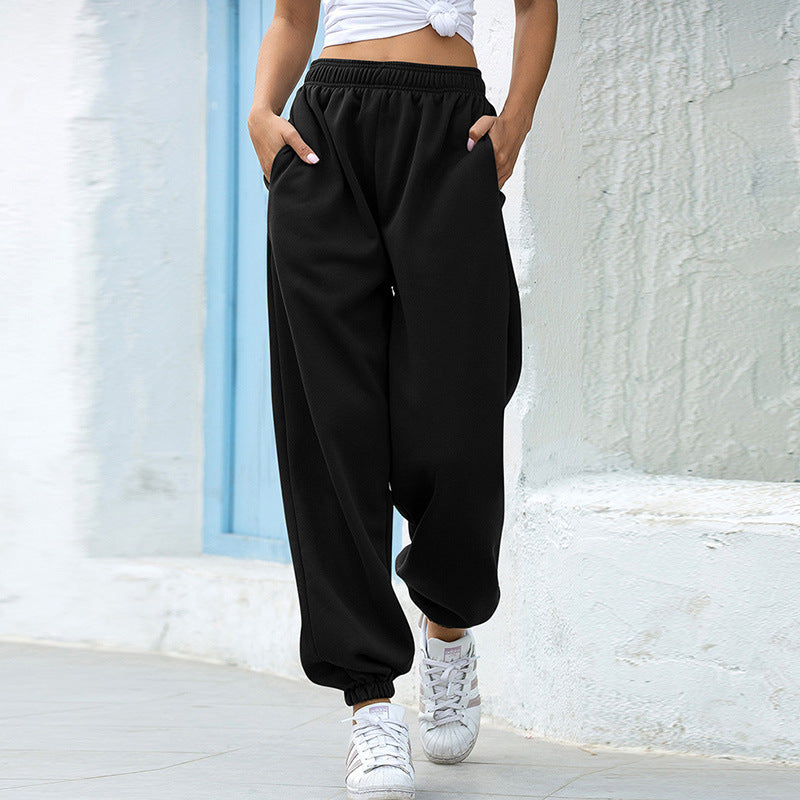 Person wearing black high-waisted pants and white sneakers against a light-colored wall.