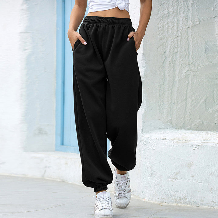 Person wearing black high-waisted pants and white sneakers against a light-colored wall.
