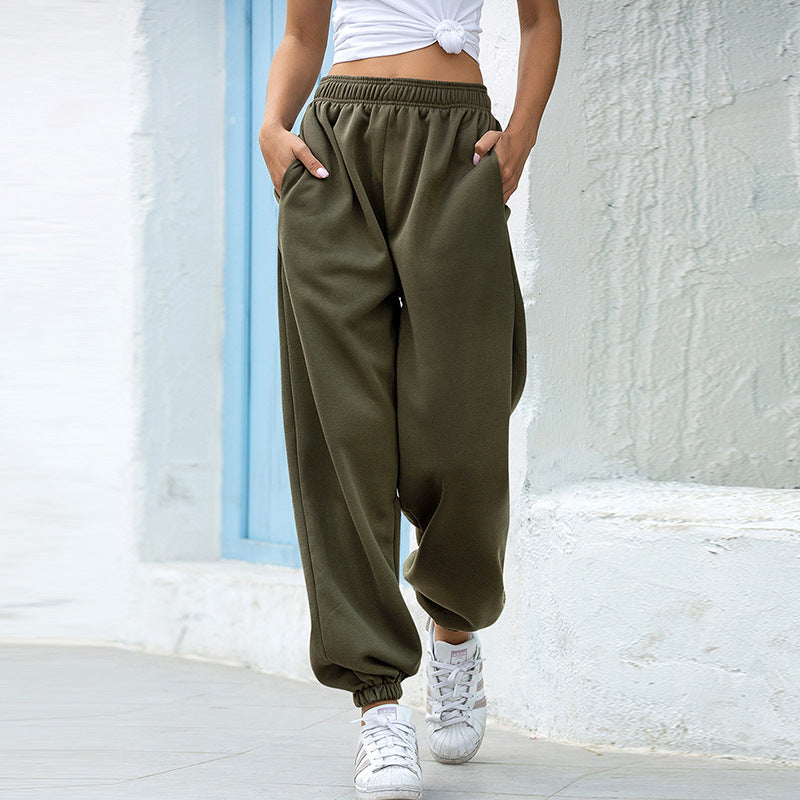Person wearing olive green sweatpants and white sneakers against a light-colored wall.