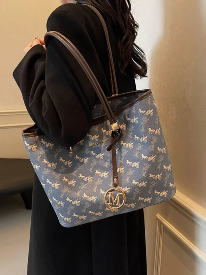 Blue handbag with horse pattern held by a person in a black outfit.