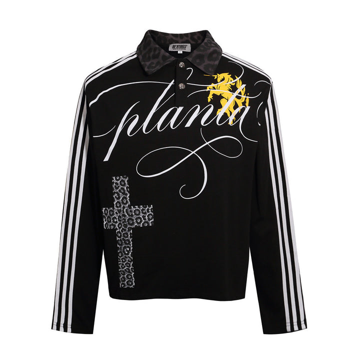 Black cross print polo shirt shown from the front with long striped sleeves, decorative lettering and a yellow chest graphic.