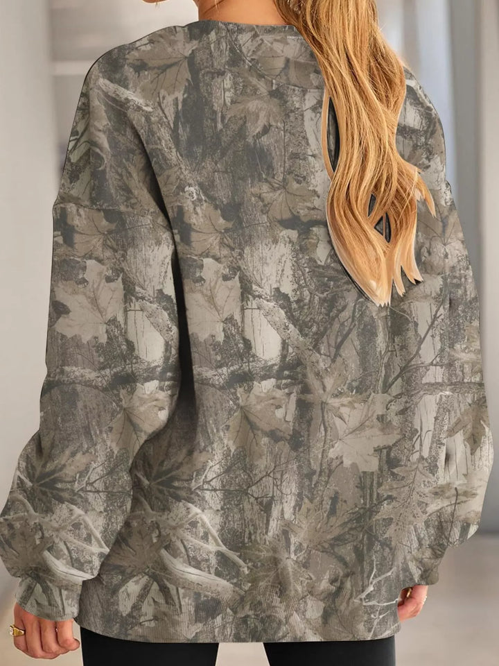 Woman in a light military green branch print sweatshirt in a rear view showing long sleeves and the back print against white.