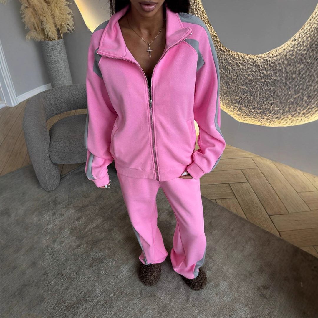 Person wearing a pink tracksuit in an indoor setting with a decorative wall and chair.