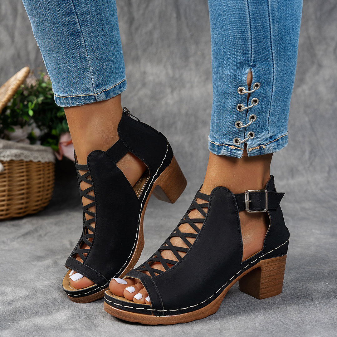 Black open-toe shoes with wooden soles worn with blue jeans on a gray background