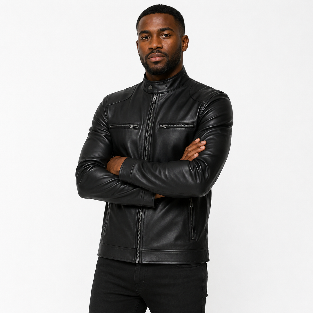 A man wearing a black leather jacket with a stand collar, zippered front, and zippered chest pockets, posed with arms crossed against a plain white studio background.