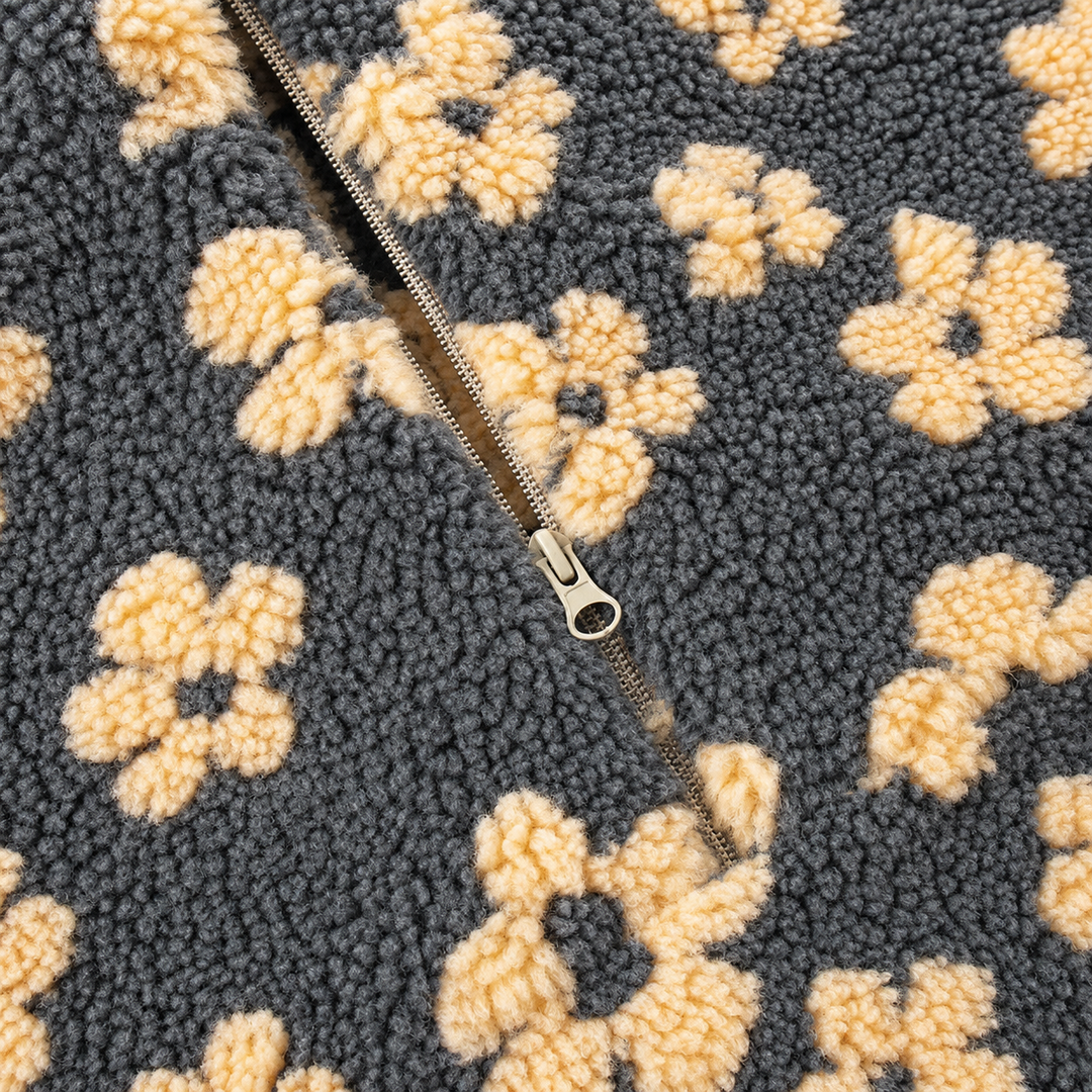 Close-up of a textured fleece or sherpa fabric with a repeating cream floral pattern on a dark charcoal background, featuring a silver metal zipper running diagonally through the center.