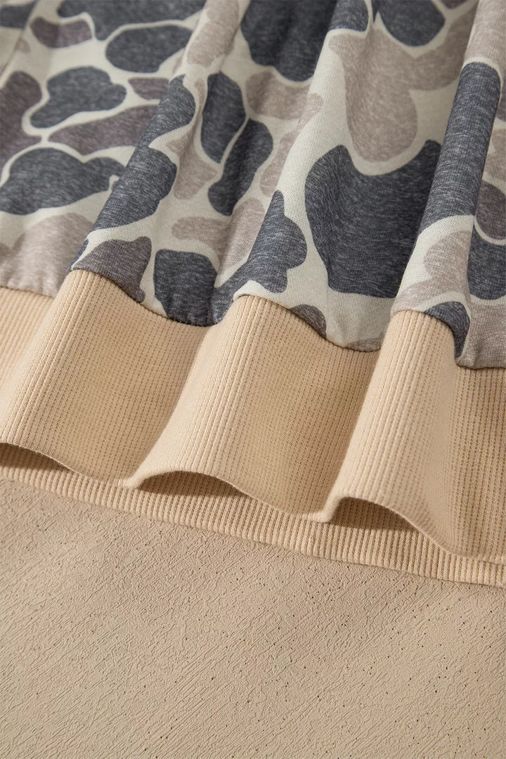 Close view of the beige ribbed bomber hem with gathered camouflage fabric above it, showing stitching and curved fabric edge.
