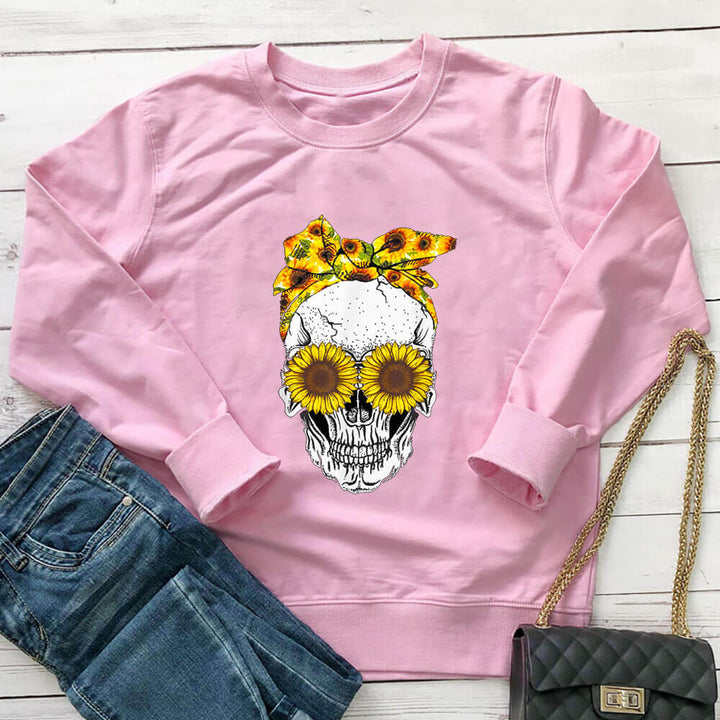 Pink sunflower skull sweatshirt laid flat with jeans and a black handbag
