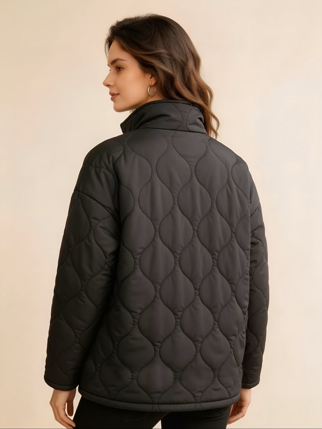 Back view of the black quilted coat on a female model showing wavy stitching, long sleeves and a straight hem below the hips.