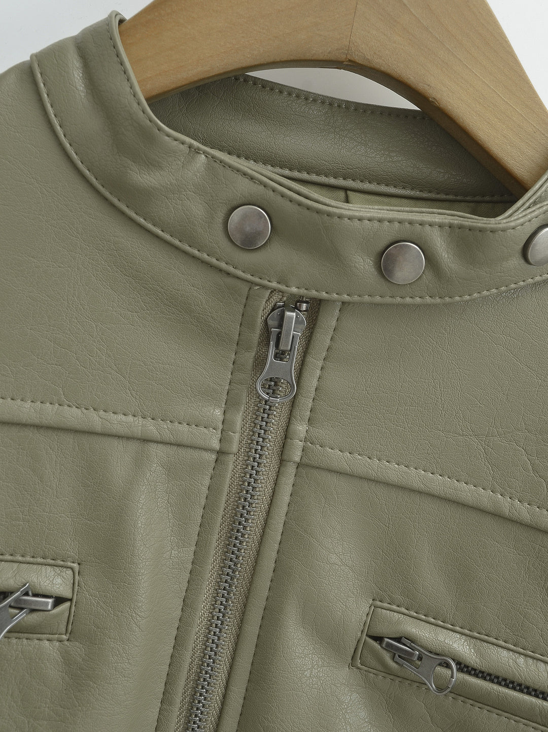 Gray Green jacket collar close-up, on a wooden hanger, with three round silver studs and front zipper detail in close detail.