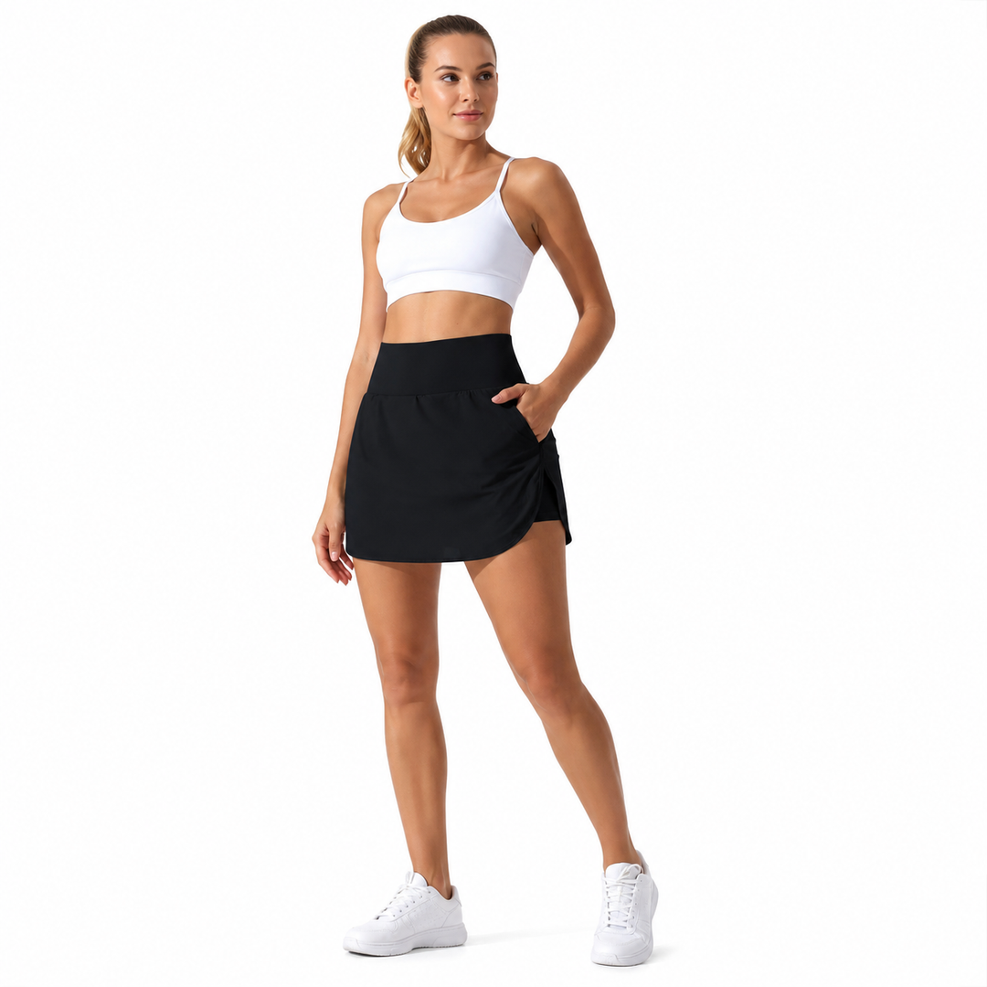 Black tennis skort women on a full-length model against white showing a high waist, side pocket and curved front overlay hem.
