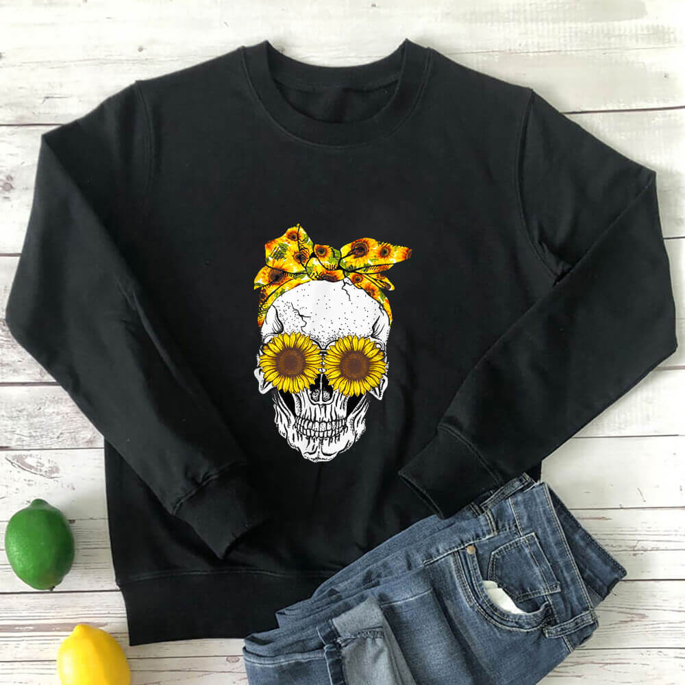 Black sunflower skull sweatshirt laid flat with jeans on a white wood background