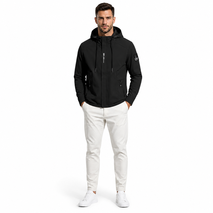 A man wearing a black hooded zip-up jacket, white pants, and white sneakers, standing against a plain white studio background.