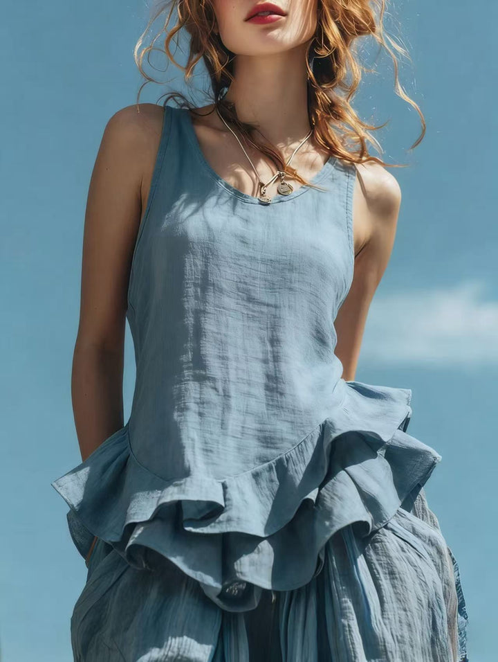 Woman wearing a light blue sleeveless dress with ruffled layers against a clear sky.