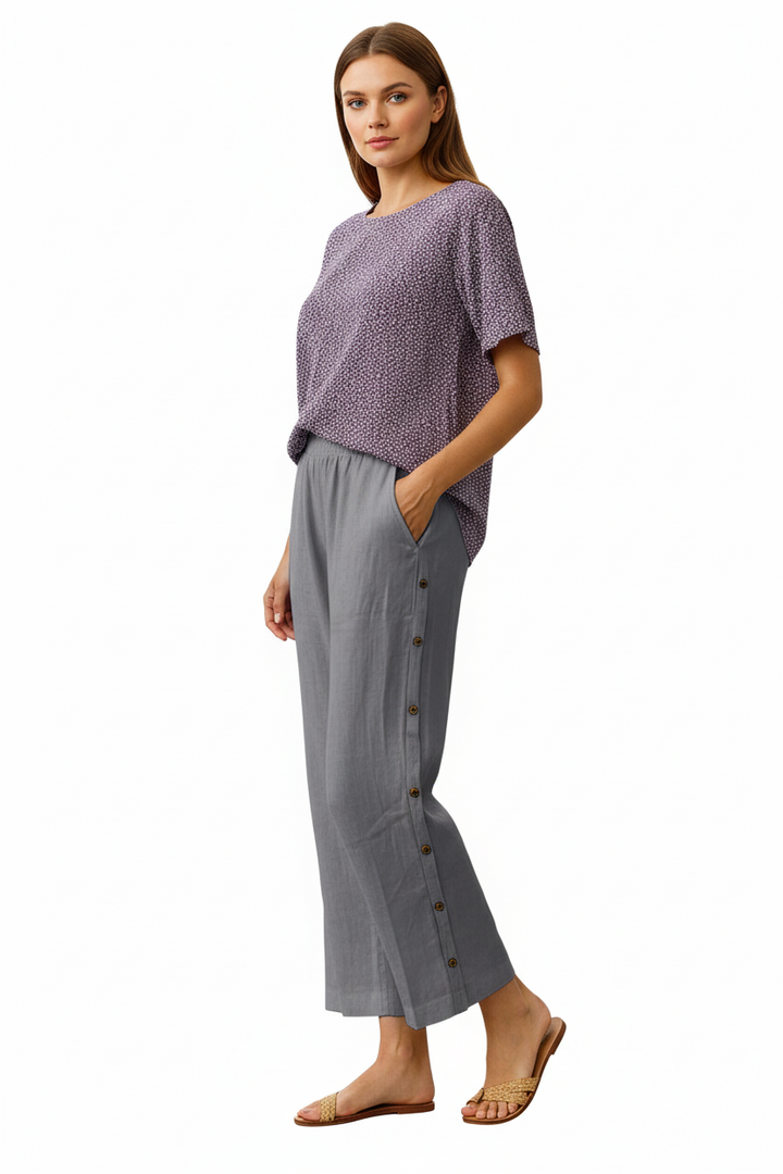 Woman wearing a patterned top and gray button-up pants on a white background