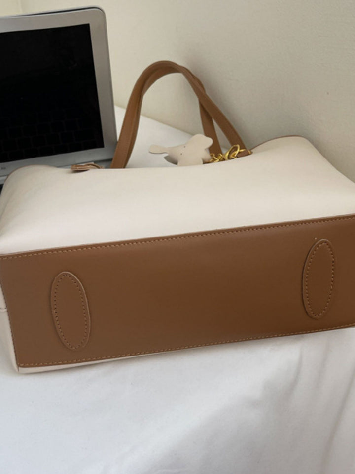 White and brown handbag on a white surface with a laptop in the background