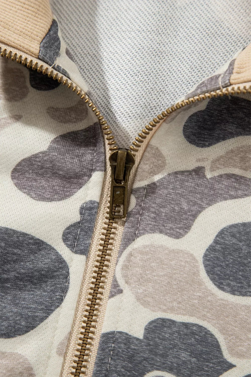 View of the open gold-tone zipper, showing the slider, zipper teeth, stitching and inside of the camouflage bomber sweatshirt