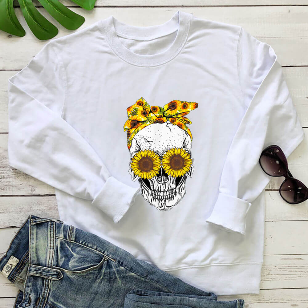 White sunflower skull sweatshirt laid flat with jeans on a white wood background