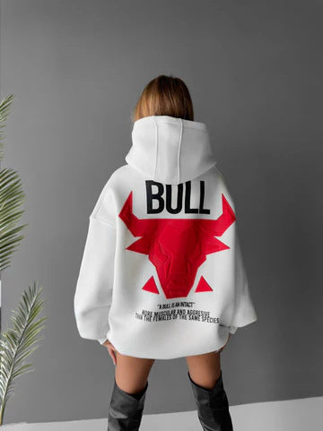 White hooded pullover shown from behind on a model, with a large red bull back graphic, long sleeves and the loose silhouette