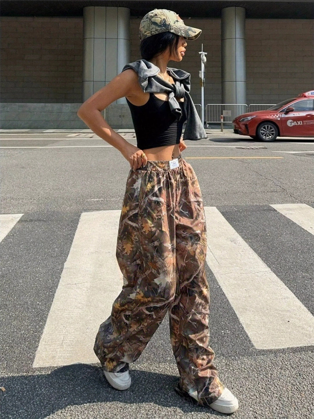 Person wearing a black crop top, camouflage pants, and a cap on an urban street.