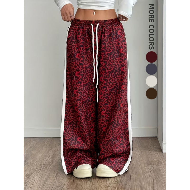 Red leopard print pants with white drawstring and side stripes on a wooden floor.