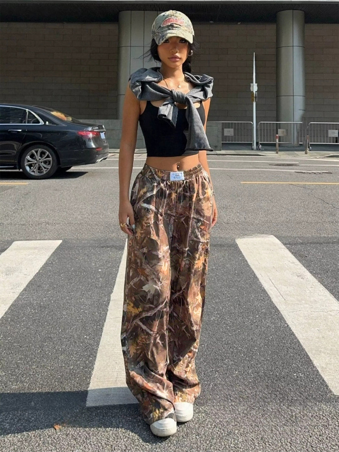 Person wearing a black crop top, gray jacket, and camouflage pants on a street.