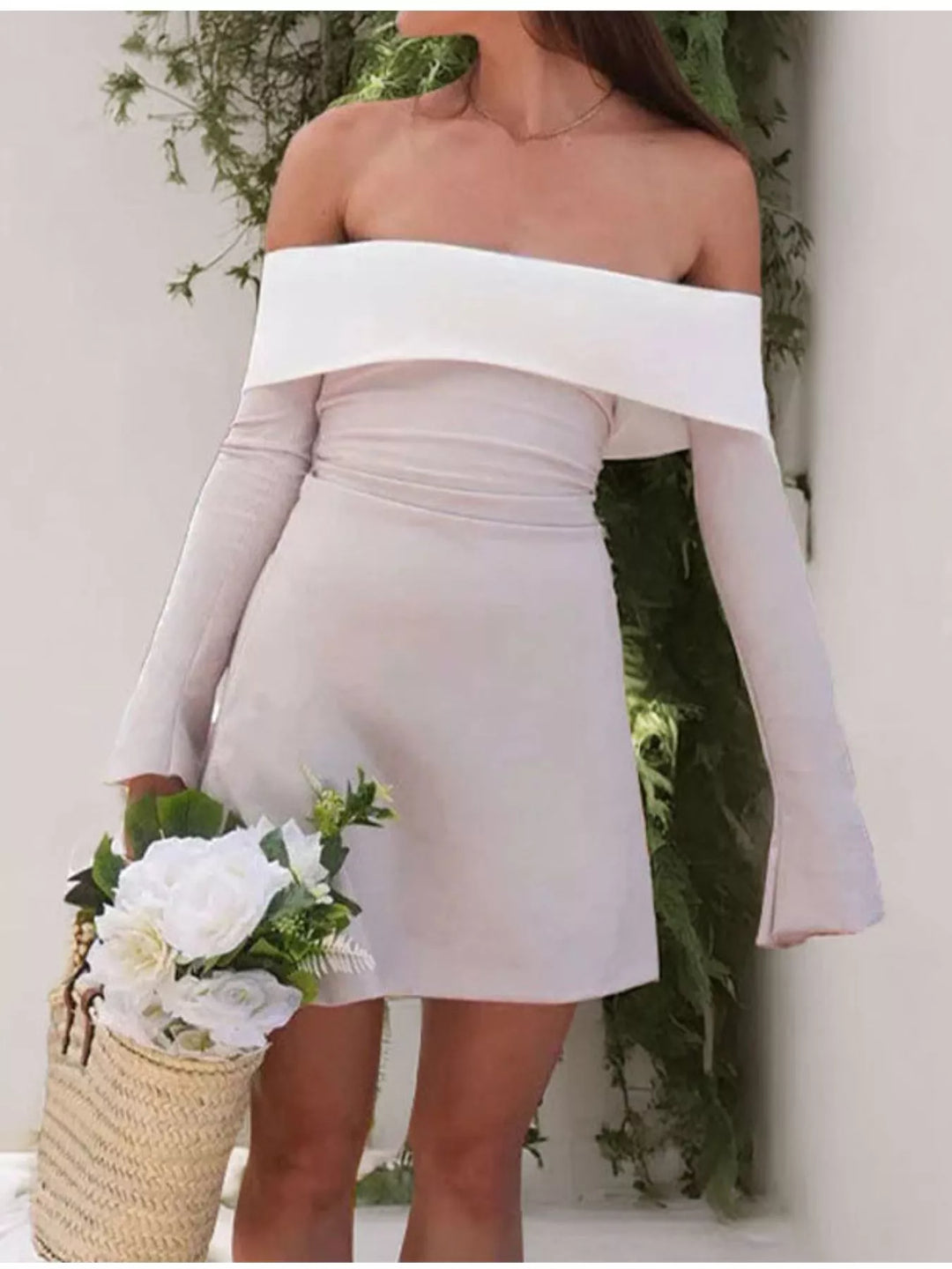 Woman wearing a white off-shoulder dress holding flowers against a neutral background
