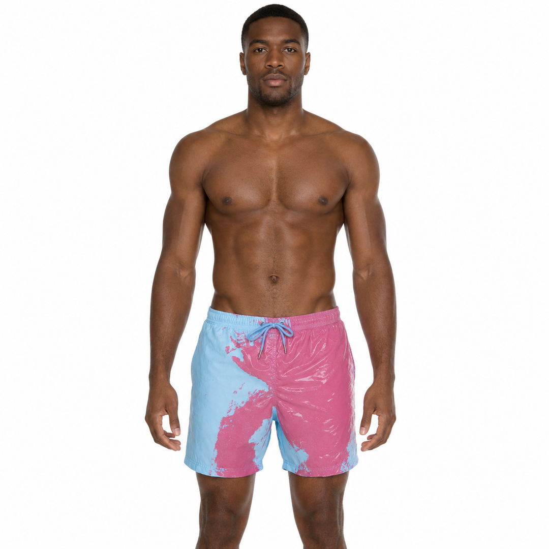 A shirtless male model wearing swim trunks with a pink and light blue paint-splatter pattern and a blue drawstring, photographed against a plain white background.