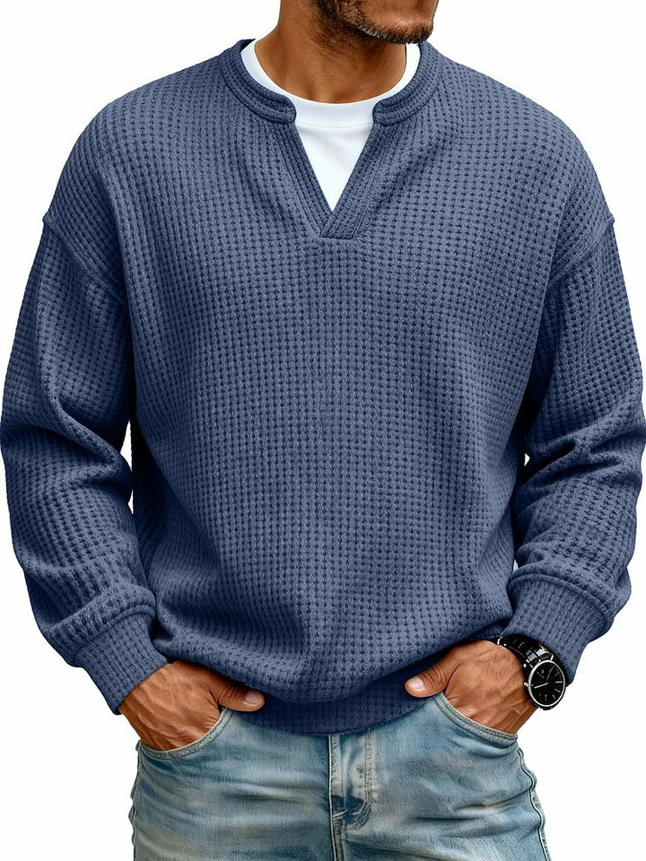 Man wearing a blue textured sweater with a white shirt underneath on a white background