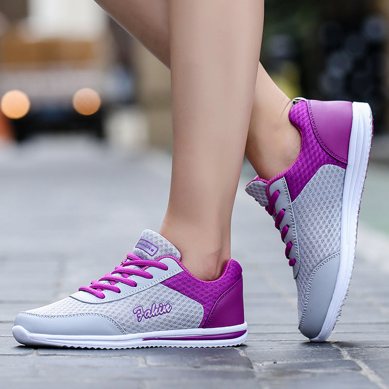 Gray and purple lace-up shoes worn outdoors, showing purple heel panels, gray mesh uppers and white soles beside stone paving