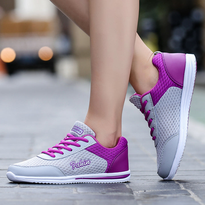 Gray and purple lace-up shoes worn outdoors, showing purple heel panels, gray mesh uppers and white soles beside stone paving