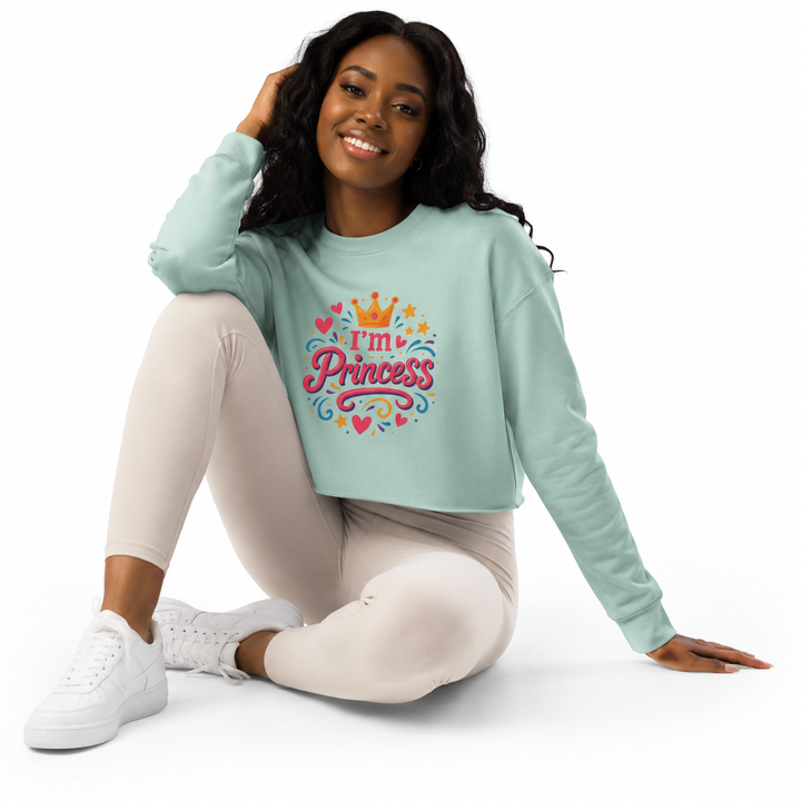 A woman sitting on a white studio floor wearing a mint green cropped sweatshirt with a colorful &
