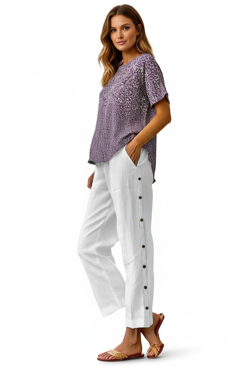 Woman wearing a purple patterned top and white pants with black buttons on a white background