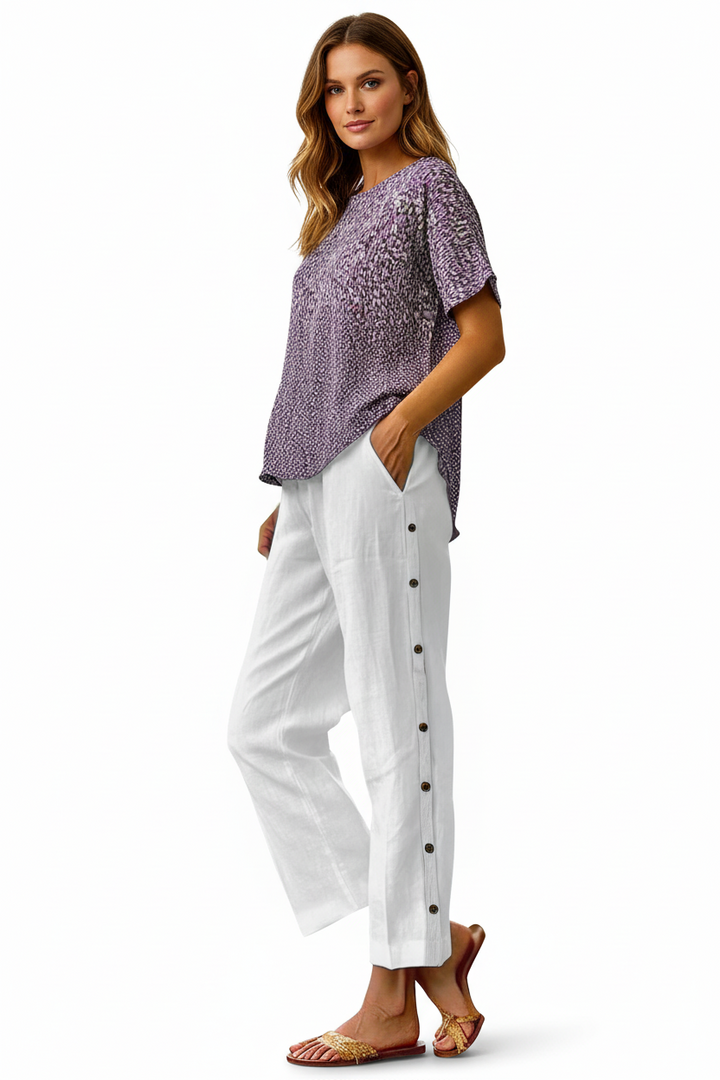 Woman wearing a purple patterned top and white pants with black buttons on a white background