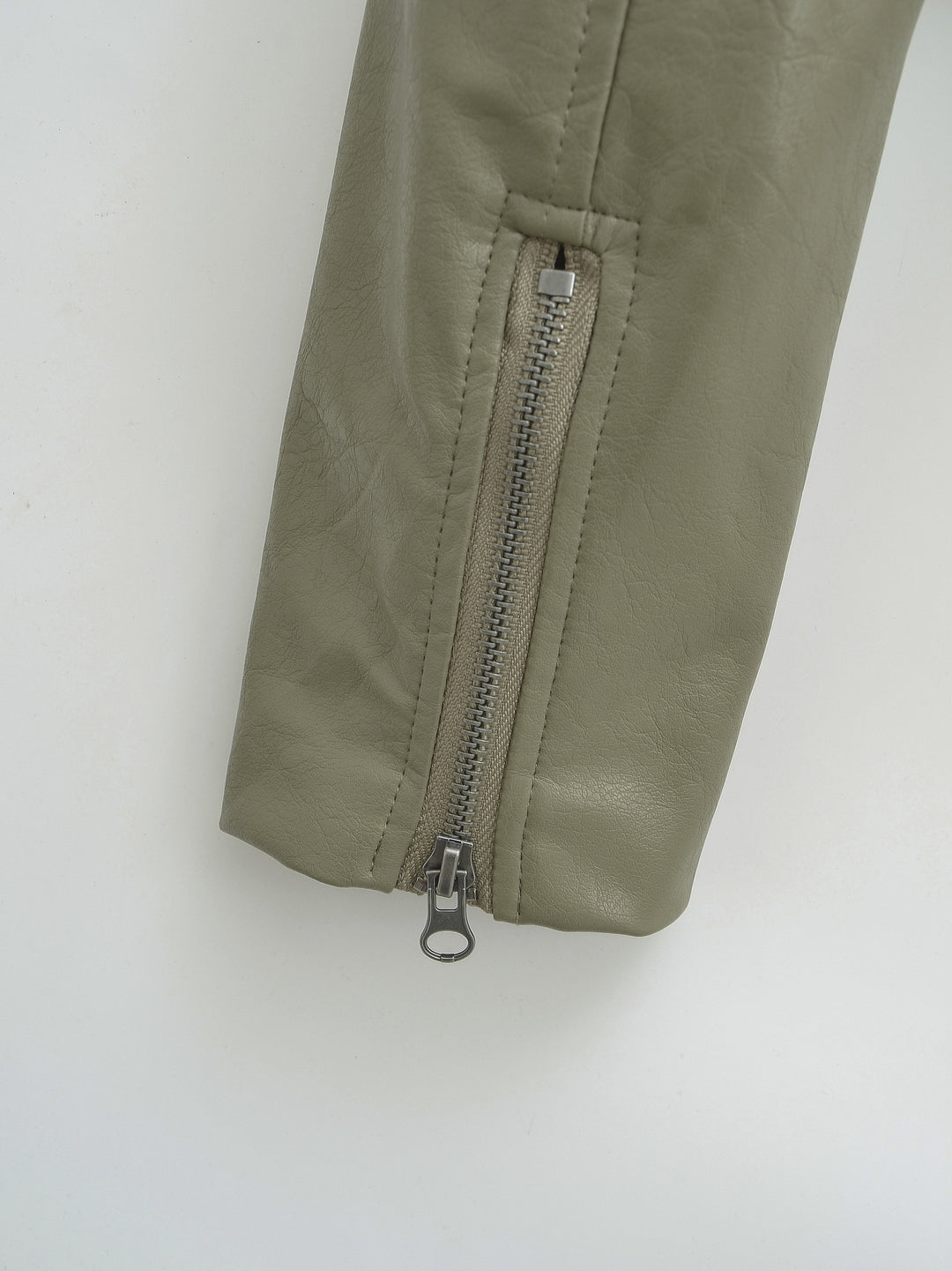 Gray Green jacket sleeve close-up showing the closed cuff zip with its silver pull and straight seam stitching against white.