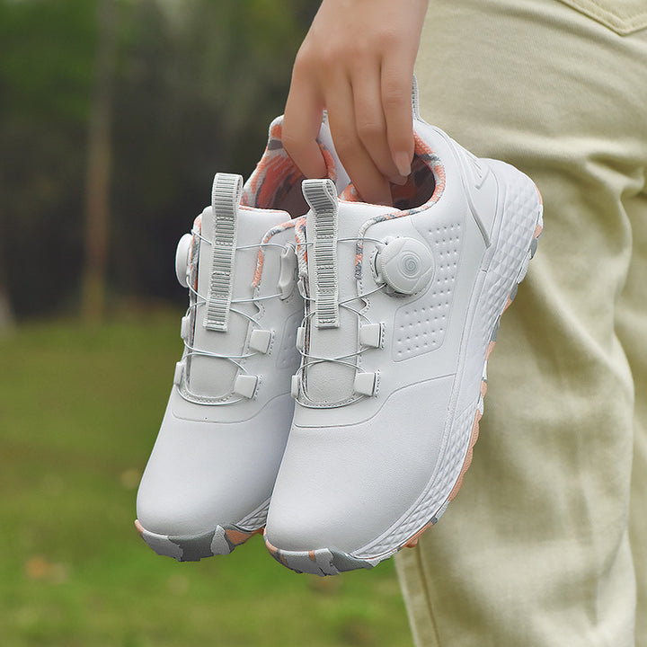 White rotary buckle footwear held by the heel loops beside light trousers, showing both shoes, side dials and cable fastening