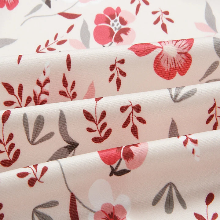 Close-up of Pink printed fabric with small red flowers, pink petals, grey leaves and scattered botanical sprigs shown folded.