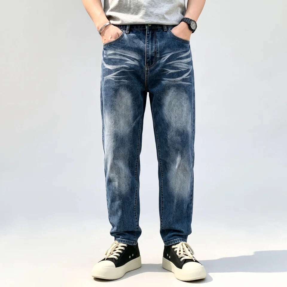 Model wearing blue vintage washed loose straight-leg denim jeans with a grey T-shirt and black sneakers, a front studio view.