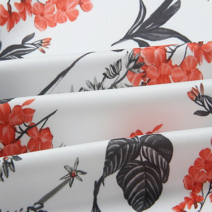 Close-up of White botanical print textile with coral-red flowers, black leaves and gray outlined floral details shown folded.