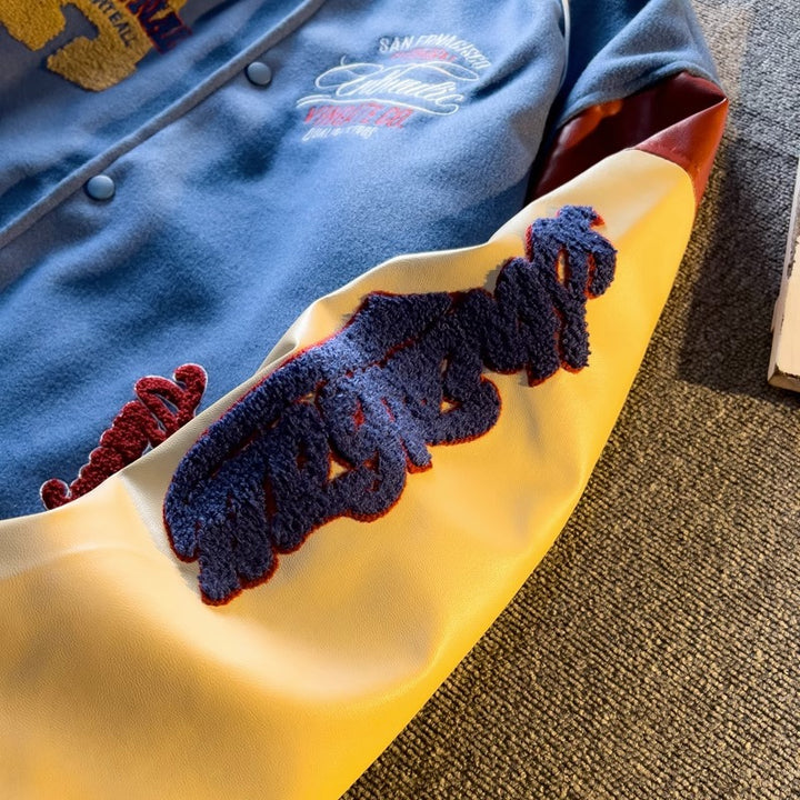 WT167 jacket in Blue shown in a close front view with sleeve embroidery and fabric details visible, on a gray fabric surface.