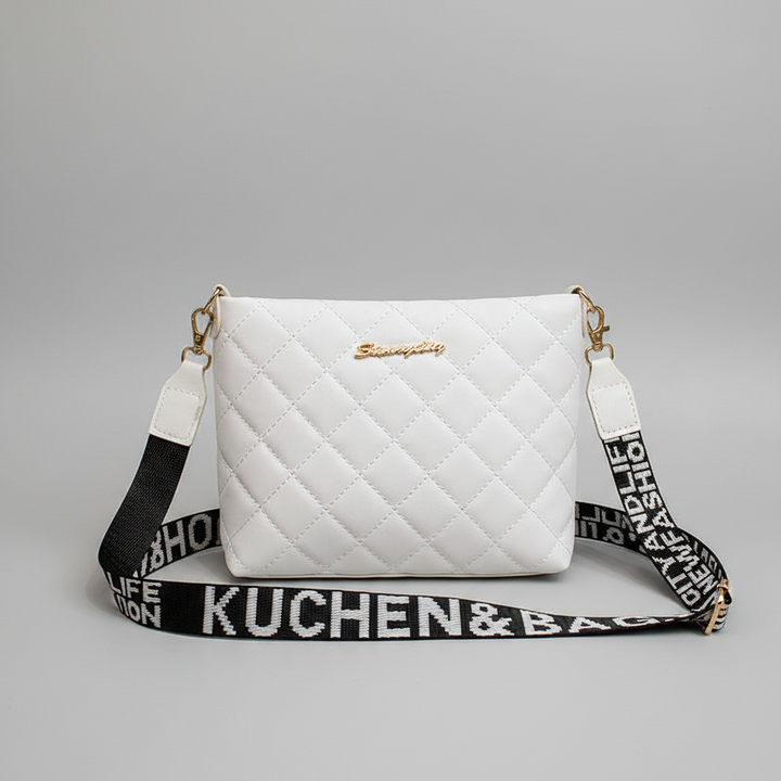 A white quilted crossbody handbag with gold-tone hardware and a black-and-white branded shoulder strap, photographed on a light gray studio background.