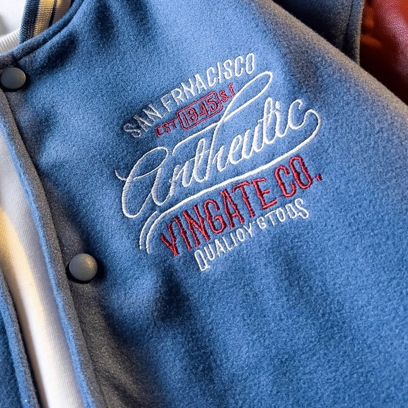 WT167 jacket in Blue shown in a close detail view, with its chest lettering and stitches visible, on a gray textured surface.