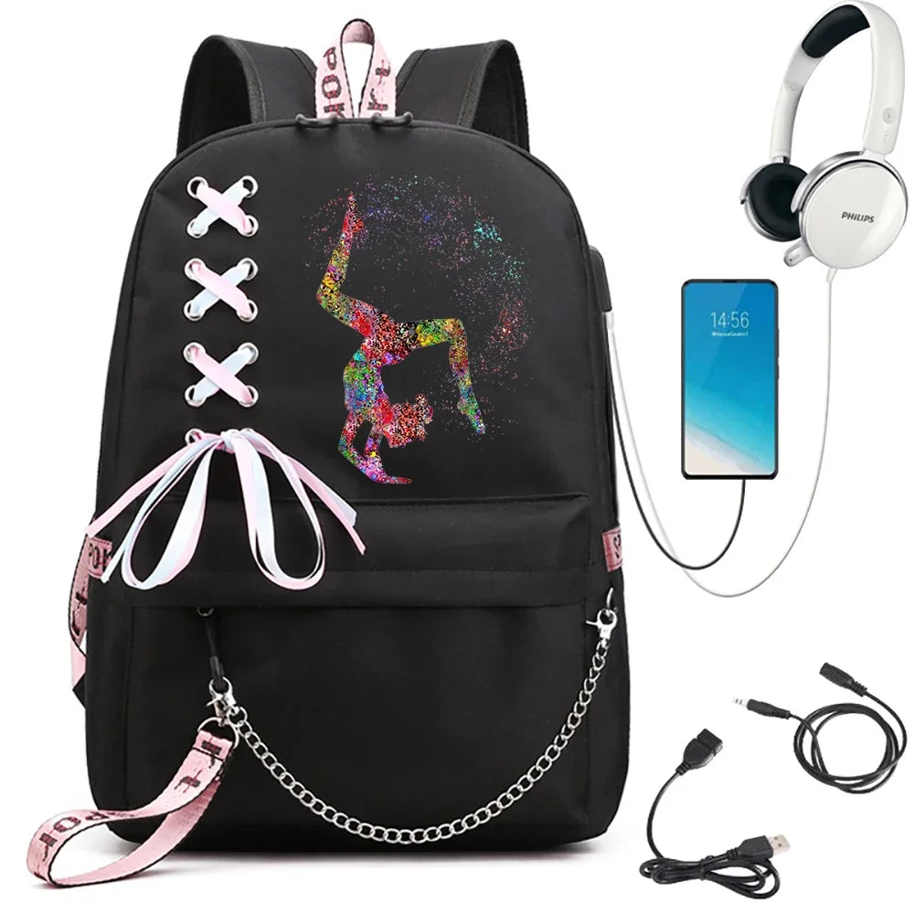 A black backpack featuring a multicolor inverted gymnast print, light pink ribbon lacing and chain, beside electronics props.