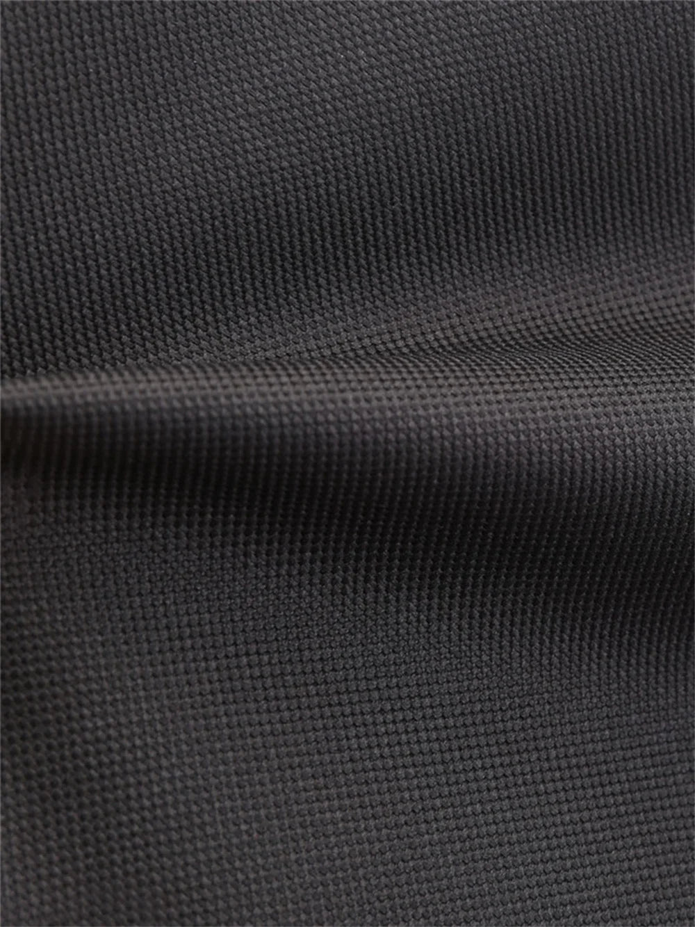 Close-up of black woven school backpack fabric, showing its visible surface grain and a softly folded seam area in the photo.